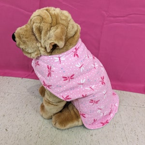 May include: A plush dog wearing a pink and white patterned shirt with a dragonfly design.
