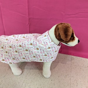 May include: A white dog wearing a pink and white dog coat with the text "I love Grandma and Grandpa" repeated on the fabric.