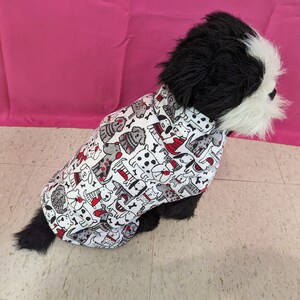 May include: A black and white dog wearing a white shirt with a red and black dog print. The shirt has a black collar.