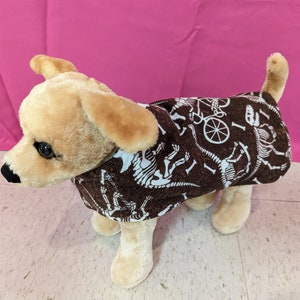 May include: A brown dog sweater with a white dinosaur skeleton print. The sweater is on a stuffed dog.