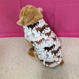 May include: A brown plush dog wearing a white and brown dog sweater with a horse print.