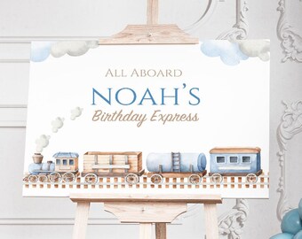 May include: A blue and white train themed birthday party sign with the text "All Aboard Noah's Birthday Express". The sign is on a wooden easel and surrounded by blue and white balloons.