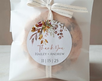 May include: A white favour bag with a brown and white ribbon tied around it. A round sticker with a watercolour floral design and the text "Thank You Hailey + Andrew 11 | 15 | 25" is attached to the bag.