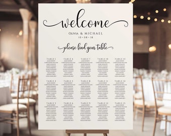 May include: A white wedding seating chart with black text. The chart is on an easel and has the words "welcome" and "Olivia & Michael" at the top. The date "10-08-18" is below the names. The chart lists the names of guests and their assigned tables.