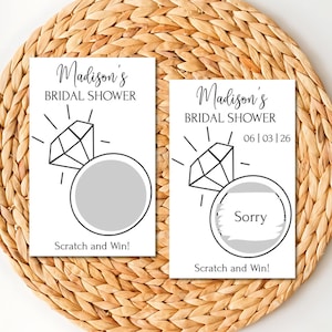 May include: Two white rectangular bridal shower scratch-off game cards featuring a black line drawing of a diamond ring. The text reads Madison's BRIDAL SHOWER, Scratch and Win!, and 06 | 03 | 26. One card shows a gray scratch-off circle, the other reveals Sorry.