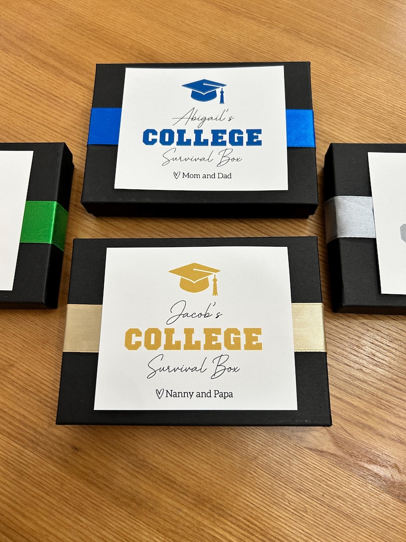 May include: Black gift boxes with white labels that read "Abigail's COLLEGE Survival Box" and "Jacob's COLLEGE Survival Box". The boxes are decorated with blue, gold, and silver ribbons. The labels include graduation cap illustrations.