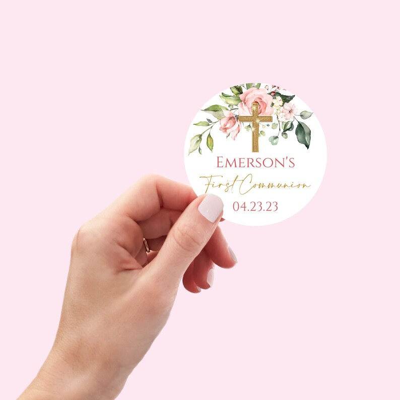 May include: Round sticker with a watercolor floral design in shades of pink and green. A gold cross is centered on the sticker. The text "EMERSON'S First Communion 04.23.23" is printed in gold and burgundy.