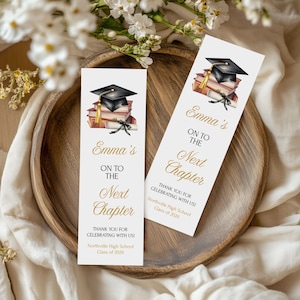 Puede incluir: Dos marcapáginas con temática de graduación con un birrete negro, libros y una ilustración de pergamino. El texto dice "Emma's On To The Next Chapter" y "Thank You For Celebrating With Us!" con el nombre de la escuela y el año de la clase.