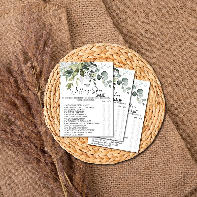 Op de afbeelding: Een printbaar bruiloftsspel met een groen en wit bloemenontwerp. Het spel heet "The Wedding Shoe Game" en vraagt ​​gasten om vragen over het stel te beantwoorden door hun schoen op te tillen.