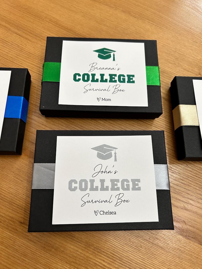 May include: Black gift boxes with white labels and ribbon accents. The labels read "College Survival Box" with a graduation cap graphic and a name. One box has green ribbon, another has silver, and a third has blue.
