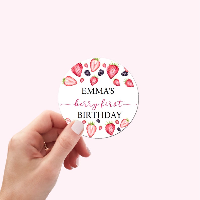 May include: A white round sticker with a red and black berry design. The text "EMMA'S berry first BIRTHDAY" is printed on the sticker.