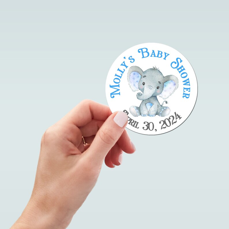 Pu&ograve; includere: Un adesivo rotondo con un'illustrazione di elefante blu e bianco. Il testo "Molly's Baby Shower" &egrave; scritto in blu intorno all'elefante. La data "April 30, 2024" &egrave; scritta in nero sotto l'elefante.