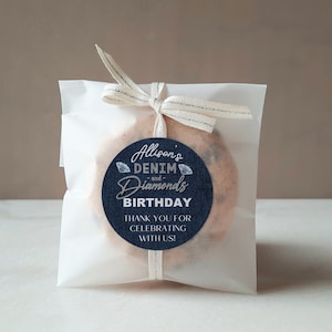 May include: A white paper bag with a blue and silver sticker that says "Alison's Denim and Diamonds Birthday Thank You for Celebrating with Us!" The bag is tied with a white ribbon.