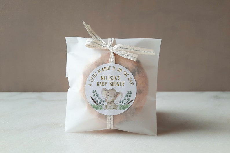 May include: A white favor bag with a gold and green sticker that says "A little peanut is on the way! Melissa's Baby Shower" with a cartoon elephant illustration.