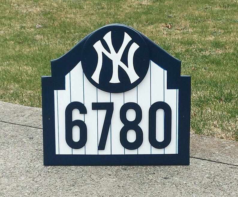 May include: A blue and white wooden house number sign with a New York Yankees logo and the number 6780.