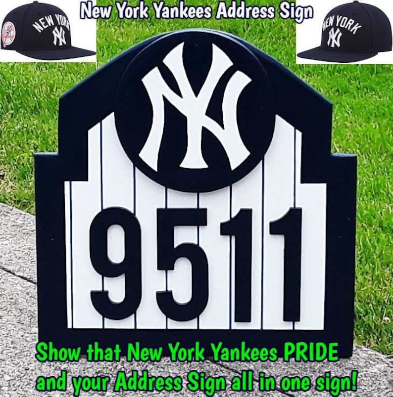 May include: A black and white New York Yankees address sign featuring the team logo and the number 9511. The sign is made of wood and has a white background with black stripes. The sign is surrounded by green grass.