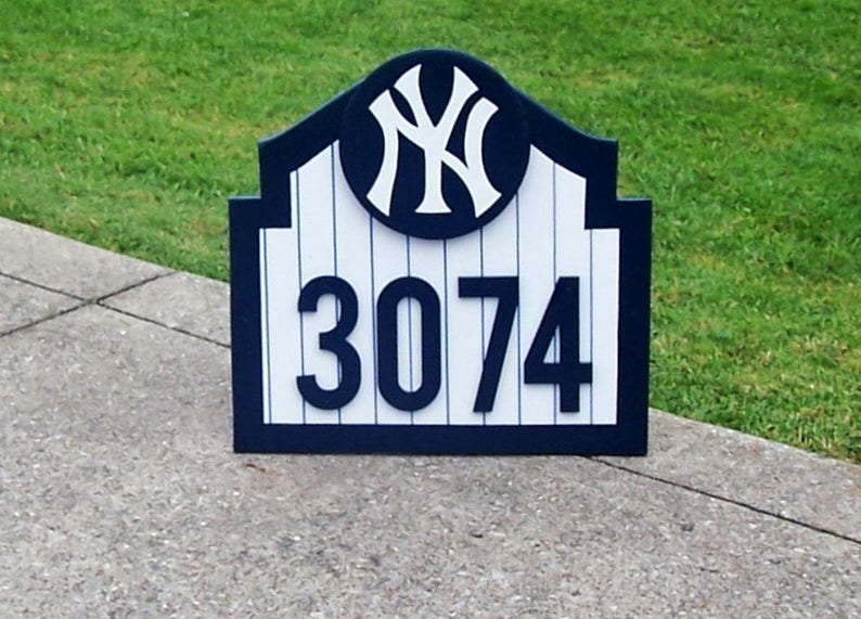 May include: A blue and white wooden sign with a New York Yankees logo and the number 3074. The sign is shaped like a baseball stadium arch.