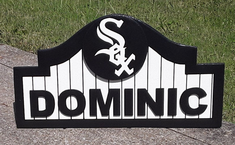 Op de afbeelding: Zwart en wit houten bord met de naam "DOMINIC". Het bord heeft het logo van de Chicago White Sox en een gebogen bovenkant. Het bord is van hout.