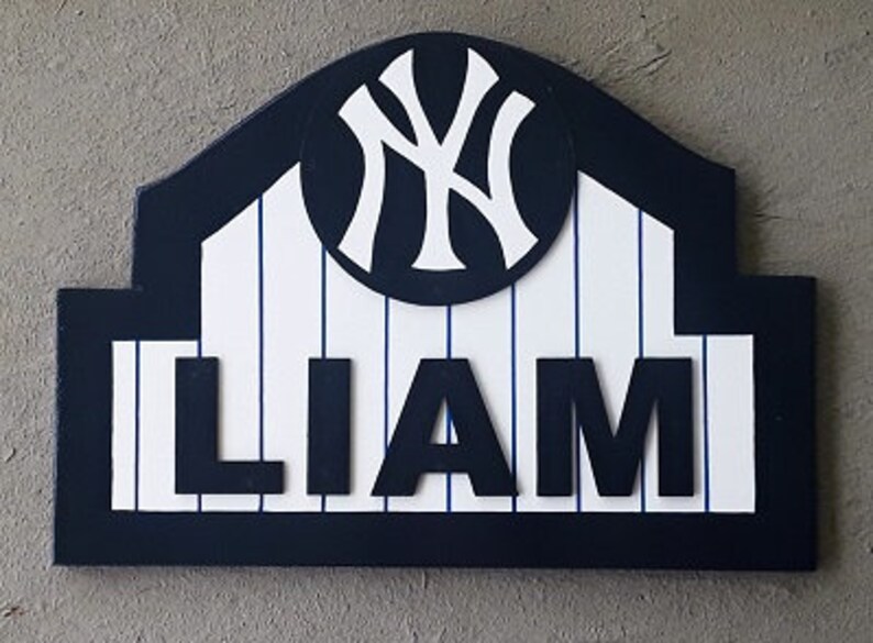 Pu&ograve; includere: Un cartello in legno con un tema da baseball blu e bianco. Il cartello presenta il logo dei New York Yankees e il nome "LIAM" in lettere bianche.