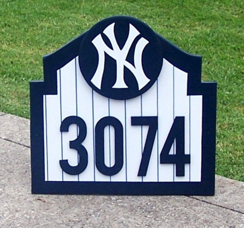 May include: A blue and white wooden sign with a New York Yankees logo and the house number 3074. The sign is shaped like a baseball stadium.