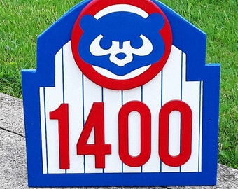 May include: A blue and red wooden sign with a white baseball-themed design. The sign features a white bear head inside a red circle with a blue background. The number 1400 is displayed in red on the sign.