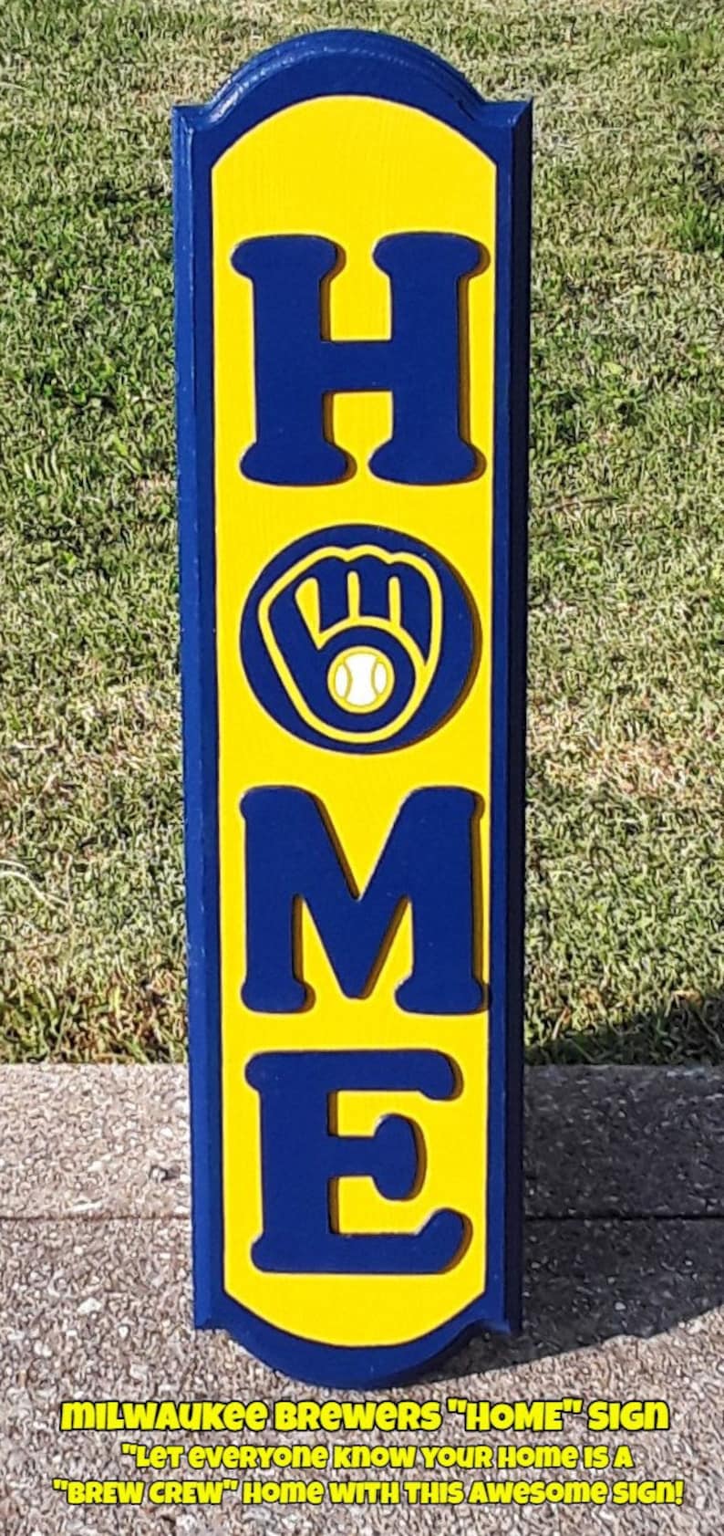 Op de afbeelding: Een geel en blauw houten bord met het woord "HOME" in grote blauwe letters. De "M" is vervangen door het logo van de Milwaukee Brewers, een blauwe handschoen met een witte honkbal. Het bord heeft de tekst "MILWAUKEE BREWERS "HOME" SIGN" en "LET EVERYONE KNOW YOUR HOME IS A "BREW CREW" HOME WITH THIS AWESOME SIGN!"
