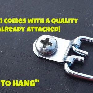 Op de afbeelding: Een close-up van een zwart houten bord met een zilveren metalen hanger eraan bevestigd. Het bord heeft de tekst "YOUR SIGN COMES WITH A QUALITY HANGER ALREADY ATTACHED!" en "READY TO HANG" in gele letters.