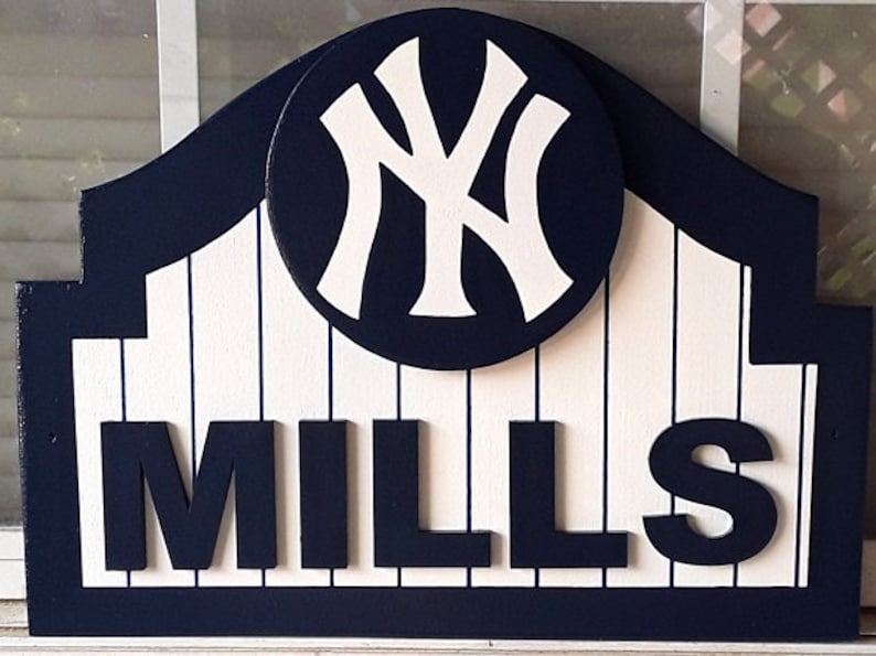 Pu&ograve; includere: Un cartello di legno con un logo dei New York Yankees blu e bianco e la parola "MILLS" in lettere bianche su sfondo blu.