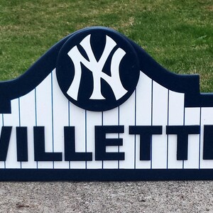 Pu&ograve; includere: Un cartello in legno blu e bianco con il logo dei New York Yankees e il nome "WILLETTTE" in lettere bianche.