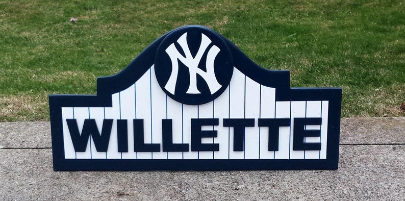 Pu&ograve; includere: Un cartello in legno blu e bianco con il logo dei New York Yankees e il nome "WILLETTTE" in lettere bianche.