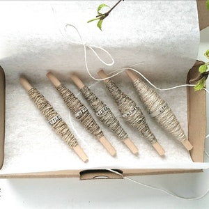 May include: Five spools of natural linen thread in a cardboard box. The spools are labeled with the word "linen" in different languages. The box is lined with white tissue paper.
