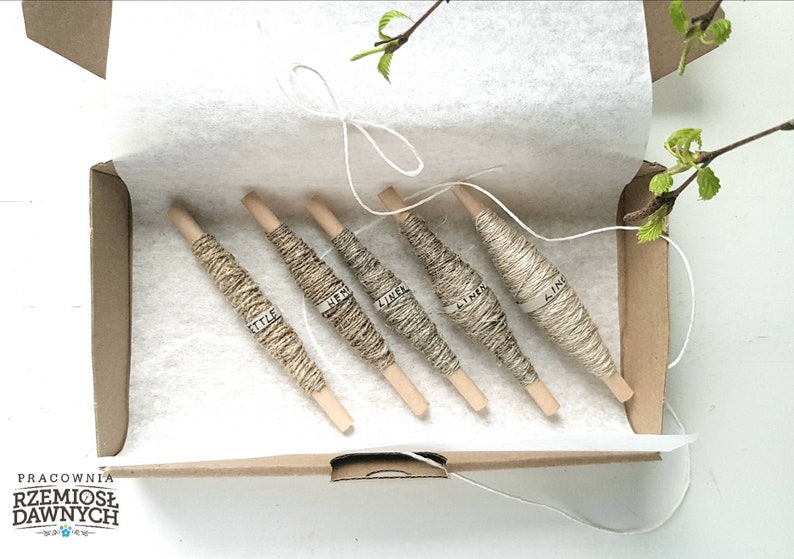 May include: Five spools of natural linen thread in a cardboard box. The spools are labeled with the word "linen" in different languages. The box is lined with white tissue paper.