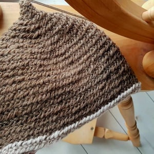 Puede incluir: Un gorro de punto marrón con un borde de ganchillo blanco. El gorro está hecho con un punto texturizado y tiene una parte superior puntiaguda.