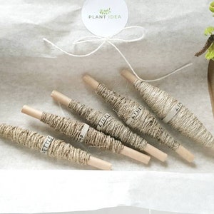 May include: Five spools of natural twine, each wrapped in brown paper with the word "Little" printed on it. The spools are arranged in a box lined with white tissue paper.