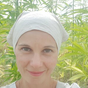 May include: A woman wearing a light gray head covering stands in a field of green hemp plants. The text "PRACOWNIA RZEMIOSŁ DAWNYCH" is visible in the upper left corner of the image.