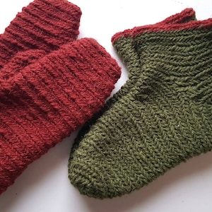 Puede incluir: Un par de calcetines de punto, uno rojo y otro verde. El calcetín rojo tiene un ribete verde y el calcetín verde tiene un ribete rojo.