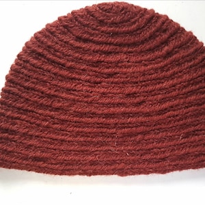 Puede incluir: Un gorro de punto rojo. El gorro está hecho de un hilo grueso y texturizado y tiene una forma simple y redondeada.