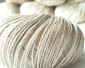 May include: A close-up of a ball of beige yarn. The yarn is made of natural fibers and has a soft, textured appearance.