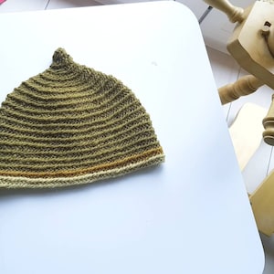 Puede incluir: Un gorro de punto de color verde con una franja marrón y crema alrededor del borde.