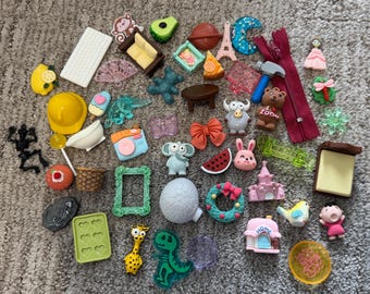 May include: A collection of assorted miniature novelty erasers in various shapes including a yellow hard hat, a brown sofa, a blue camera, a red zipper, a green picture frame, a pink castle, a giraffe, a skeleton, and various food and animal figures.