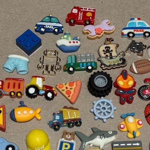 May include: A collection of colorful, miniature novelty embellishments in various shapes. Includes a blue taxi, red fire truck, police car, boat, robot, pizza slice, and a yellow submarine. Other shapes include a tractor, airplane, and a football.