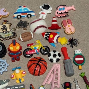 May include: A collection of colorful resin embellishments in various shapes. Includes a police car, astronaut, baseball, football, rocket ship, bicycle, basketball, soccer ball, and more. Perfect for crafting and scrapbooking projects.