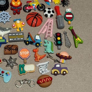 May include: A collection of colorful, miniature charms in various shapes. Includes a basketball, soccer ball, airplane, dinosaur, stop sign, and a guitar. Other charms include a car, a hamburger, and a pair of handcuffs.