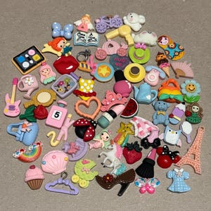 May include: A collection of colorful resin charms in various shapes, including a guitar, cupcake, Eiffel Tower, and high heel. Other charms include a ladybug, butterfly, and a dress. The charms are in shades of pink, blue, yellow, and red.