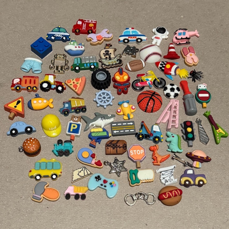 May include: A collection of colorful, miniature decorative charms in various shapes. The charms include a fire truck, a baseball, a dinosaur, a stop sign, a hamburger, a video game controller, and a basketball. The charms are made of plastic.