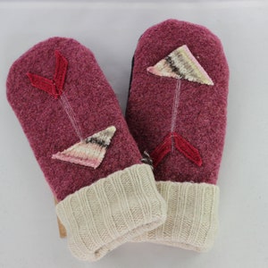 May include: A pair of pink wool mittens with white and pink arrow designs. The mittens have a white knit cuff.