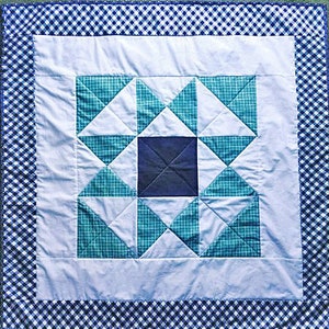 Può includere: Una trapunta patchwork blu e bianca con un bordo a quadri. La trapunta è composta da quadrati e triangoli in tonalità di blu e bianco.