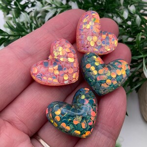 May include: Four heart-shaped resin charms with iridescent glitter embedded in the resin. The charms are pink, teal, and green.