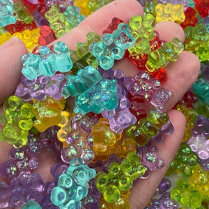 May include: A collection of colourful gummy bear charms with iridescent glitter. The gummy bears are in various shades of green, blue, purple, yellow, and red.