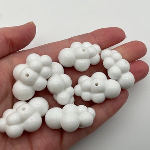 May include: A set of eight white ceramic cloud-shaped beads. The beads are all different sizes and shapes, and they have a smooth, glossy finish.